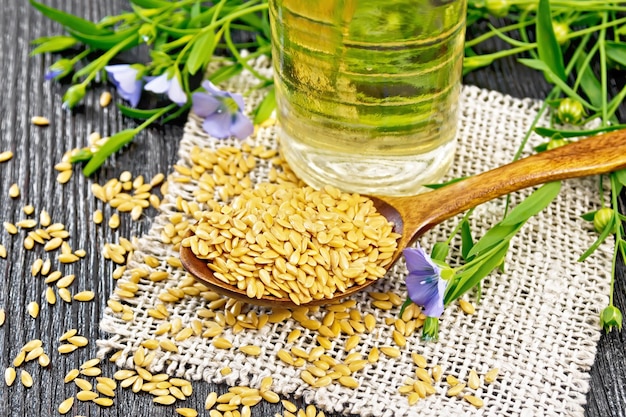 White linen seeds in a spoon flax stalks with blue flowers and green leaves on burlap oil in a bottle on black wooden board background