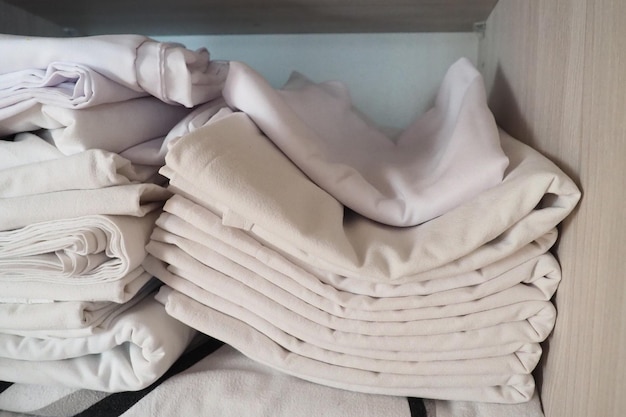 The white linens are stacked in the closet internal contents of\
a linen closet household organization hygienic conditions for sleep\
fabrics and bed sheets in half open white closet or wardrobe