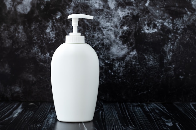 White liquid soap on black marble background in bathroom. Dispenser bottle.