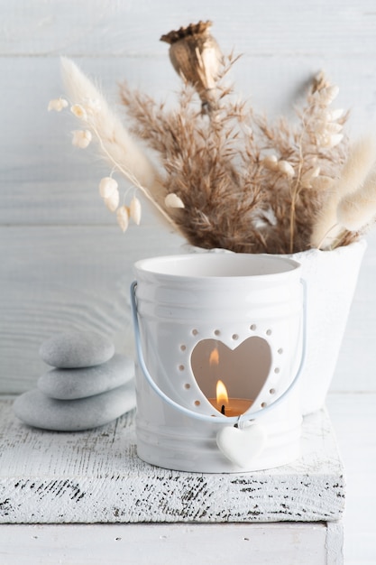 White lit aroma candle and golden dry flowers on rustic table. Greeting card for wedding or celebretion in monochrome style