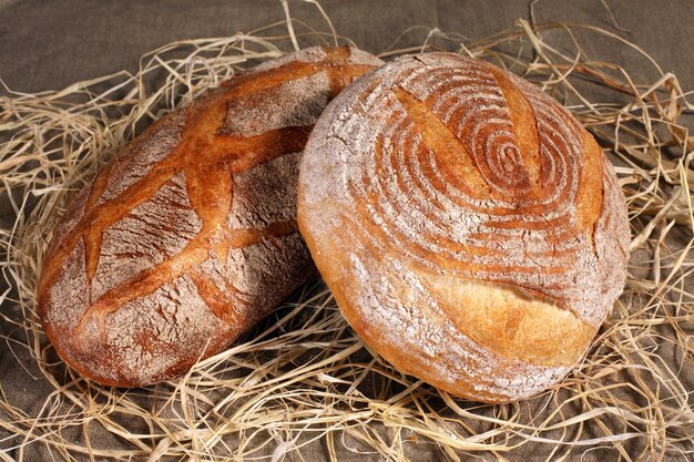 White loaf two different forms lying in the straw on gray linen tablecloth