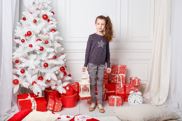 White long haired girl decorates a room with Christmas toys. A little girl and a Christmas tree