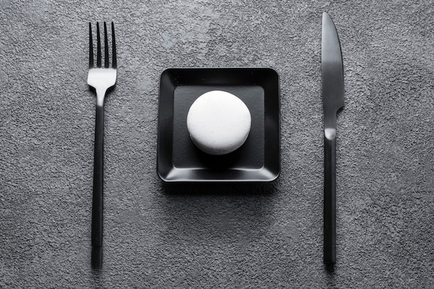 White macaroni cake in a black square plate. beautiful composition, minimalism, geometric central arrangement, table setting.