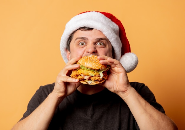 White man in black T-shirt and Santa Claus hat with burger on yellow wall