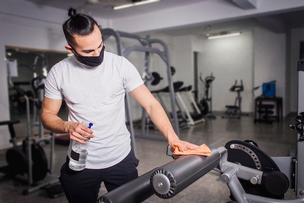 Uomo bianco che disinfetta le macchine per esercizi per le gambe.