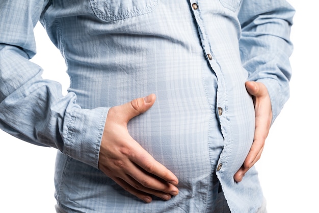 A white man is standing against an isolated wall, only his belly and arms are visible.