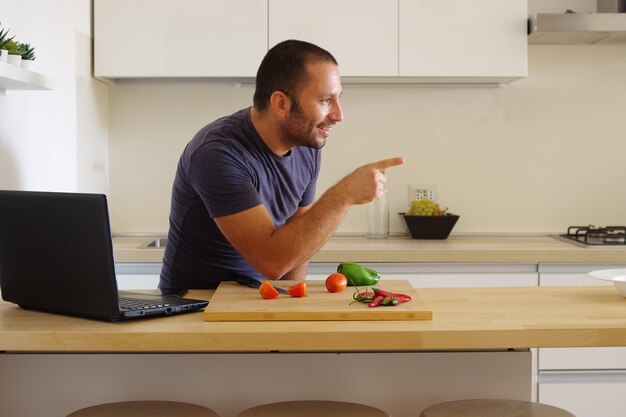 White man pointing at nothing while preparing vegetables on a wooden board in the kitchen