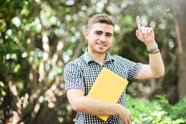 庭の黄色の本で笑って白い男学生の幸福