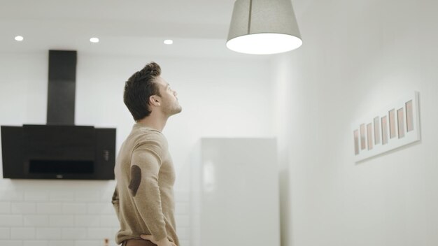 Photo white man switching off chandelier at kitchen young guy twisting up light bulb