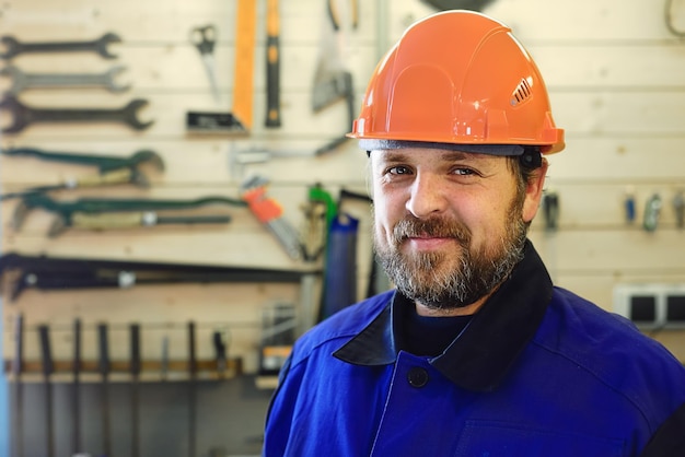 A white man with a beard in an orange helmet and working clothes on the background of a stand with tools is smiling and looking directly at the camera Layout