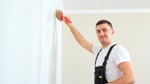 White man worker in overalls do repair glue walk under the wallpaper or primer on wall