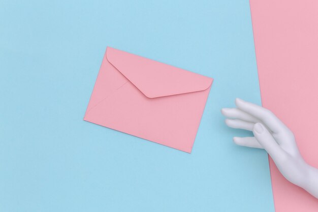 White mannequin hand and envelope on pink blue pastel background. Top view