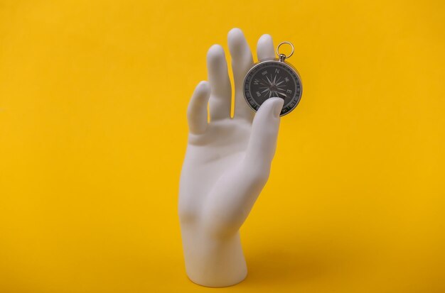 White mannequin hand holding compass on yellow background.