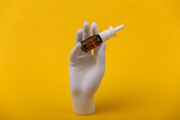 White mannequin hand holding nasal spray on yellow background.