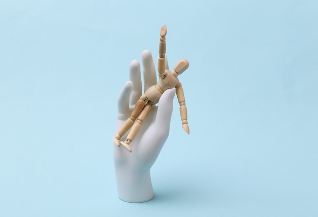 White mannequin hand holds wooden puppet on blue background