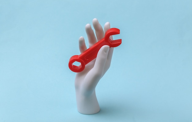 White mannequin hand holds wrench on blue background. Renovation concept, industry. Minimalism