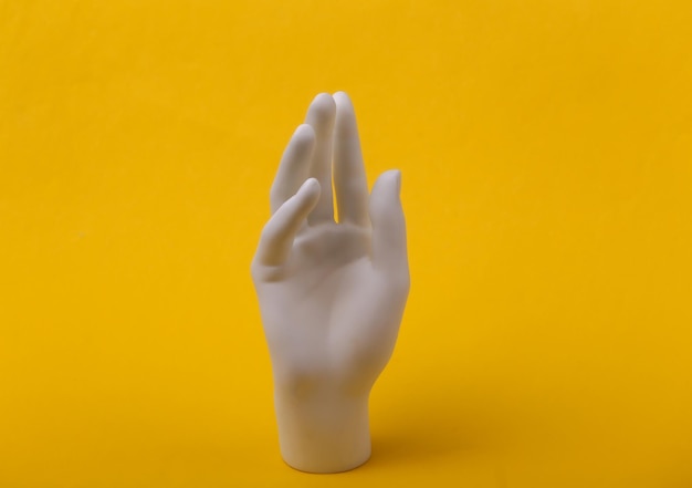 White mannequin hand on yellow background. Minimalism fashion concept