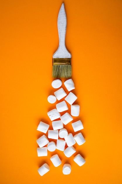 White marshmallows on yellow background with painting brush. creative concept of unheathy junk food. food sweets background