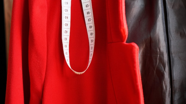 Nastro di misurazione bianco sullo sfondo del tessuto rosso della giacca. concetto di vestiti da cucire