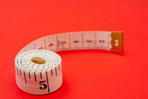 White measuring tape on red background. Measurement of length and circumference. Lose weight and get fat.