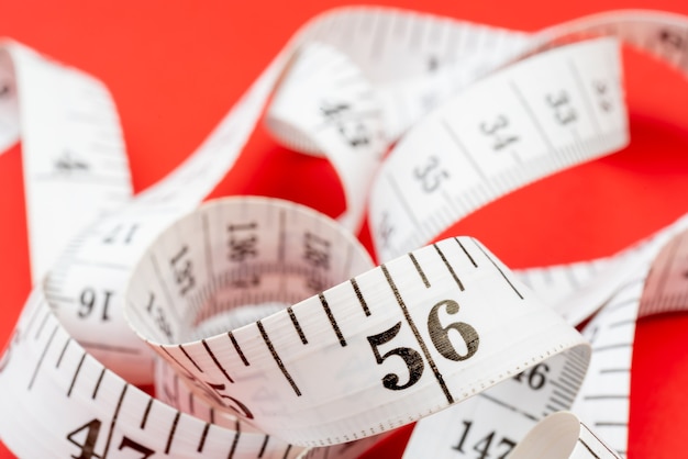 White measuring tape on red background. Measurement of length and circumference. Lose weight and get fat.