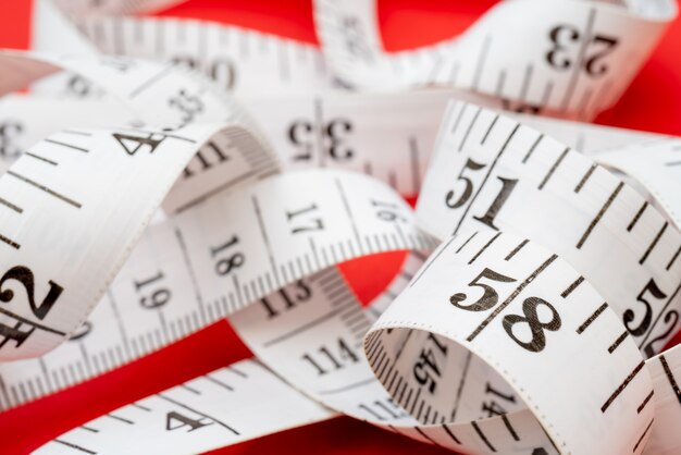 White measuring tape on red background. Measurement of length and circumference. Lose weight and get fat.