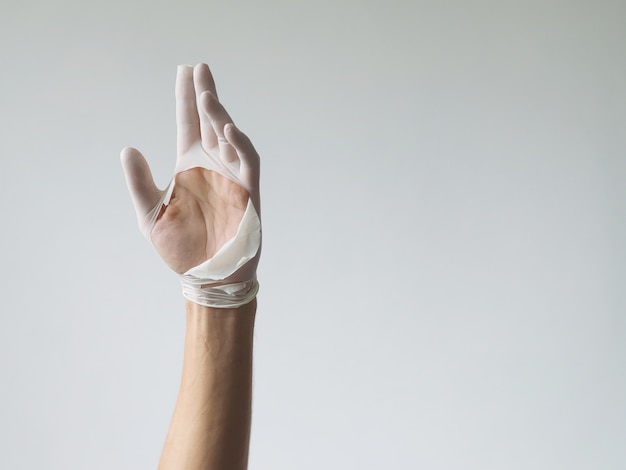 White medical glove in hand on white wall background.