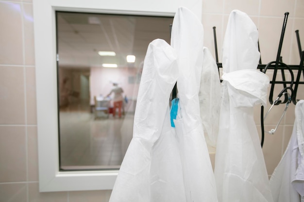 White medical gowns hang on hangers in the hospital