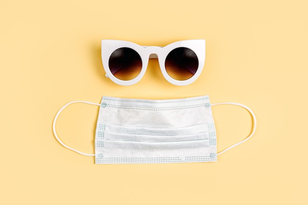 Белая медицинская маска и солнцезащитные очки на желтом фоне. Маска для защиты от вирусов, гриппа, коронавируса, COVID-19. Медицинское оборудование.