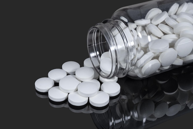 Белые медицинские таблетки в пластиковом флаконе на темном фоне Здравоохранение и лекарства