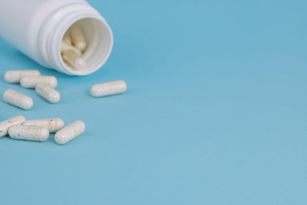 White medical pills spilling out of bottle on a blue background