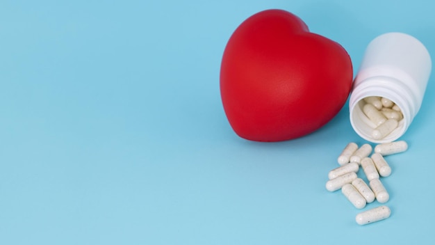 Foto pillole mediche bianche che fuoriescono dalla bottiglia e dal cuore rosso su sfondo blu con spazio per la copia