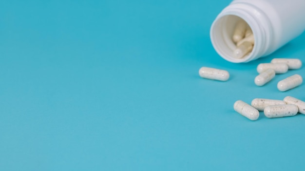 Фото Белые медицинские таблетки, выливающиеся из бутылки на синем фоне