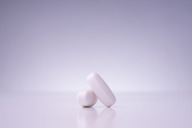 Белые медицинские таблетки на белом столе с отражением
