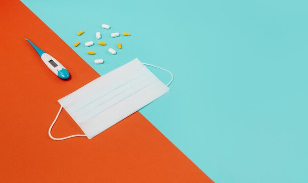 White medical protective mask, with pills and thermometer on blue.