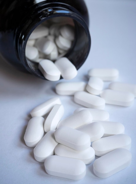White medicinal pills are scattered from a bottle container close-up