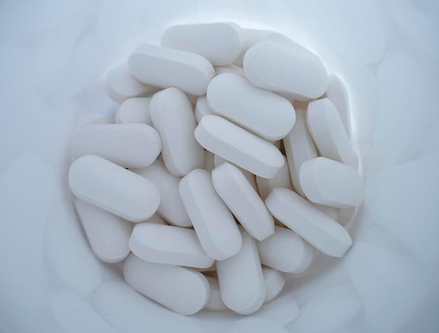 White medicinal pills are scattered from a White bottle container close-up