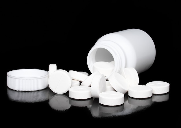Bottiglia bianca della medicina, pillole di colore su fondo nero.