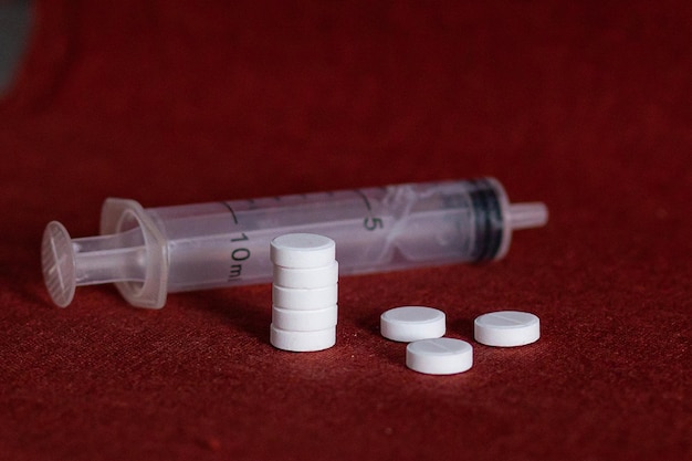Белые таблетки и шприц лежат на бордовом фоне врачи дня здоровья и лекарства принимают витамины лечение болезней