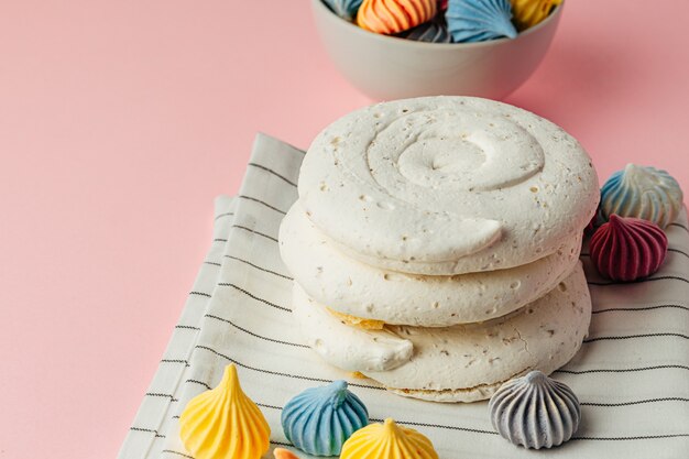 White meringue cookie on pink background with colorful mini meringues 