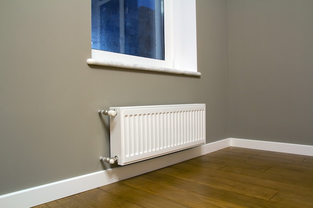 White metal heating radiator mounted on gray wall inside a room