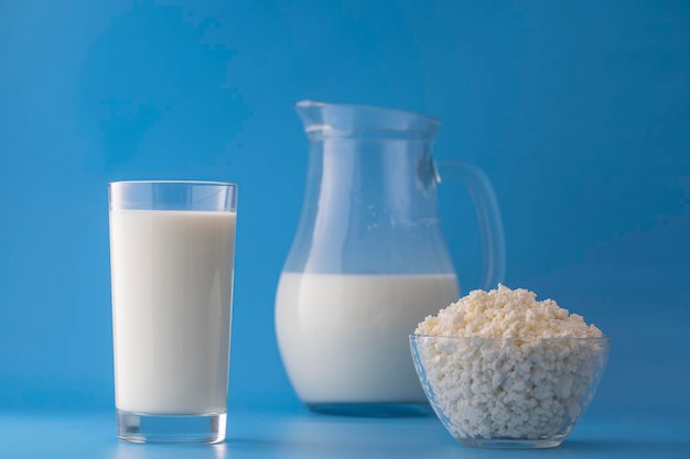 White milk in a jug and glass and cottage cheese on a blue background Dairy product concept