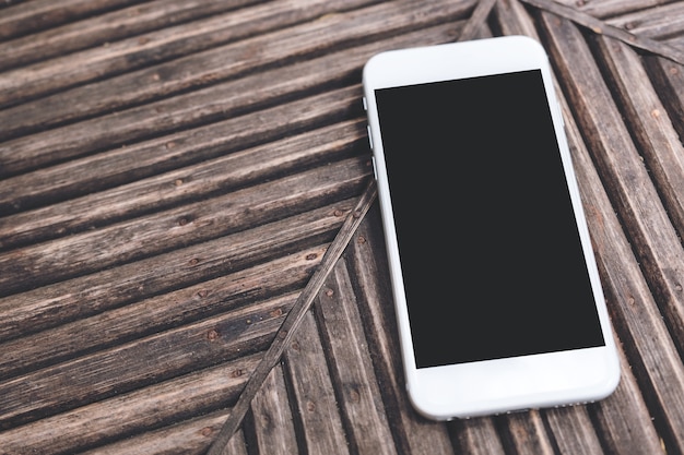 Foto un telefono cellulare bianco con schermo desktop nero bianco su sfondo di tavolo in legno d'epoca