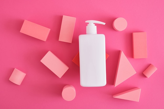 White mock up cosmetic bottle with dispenser and geometric shapes forms. Exhibition podium, platform for product presentation on pink background. top view