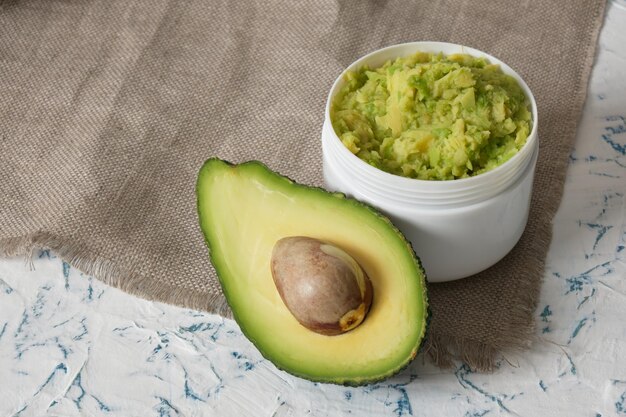 White mockup plastic jar with avocado puree cut in half avocado and wooden comb