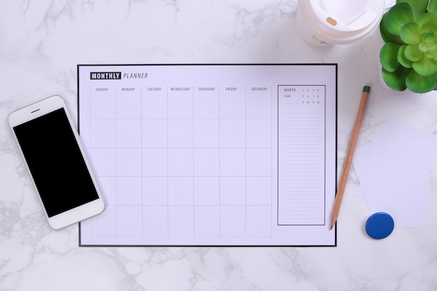 White mockup smartphone and planner schedule on marble background