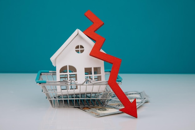Foto modello bianco della casa nel carrello con la freccia in giù che cade dei prezzi del mercato immobiliare