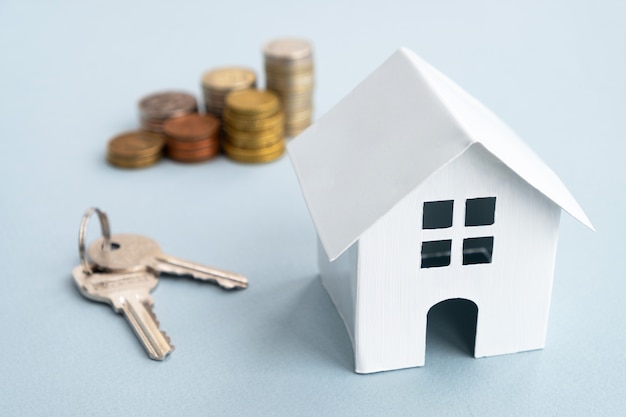 white model house, keys and stack coins on light wall