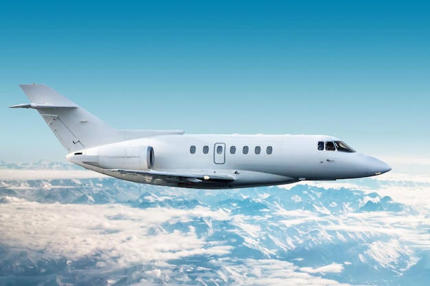 White modern corporate aircraft flies over snow covered mountains