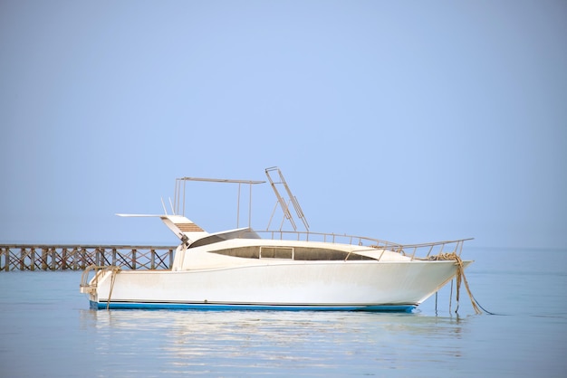 La barca a motore bianca galleggia nell'acqua dell'oceano sul lungo ponte del molo sotto il cielo blu brillante vista dalla spiaggia sabbiosa concetto di viaggio estivo